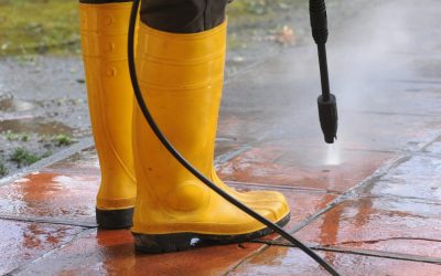 A person wearing yellow rubber boots with high-pressure water nozzle cleaning the dirt in the tiles
